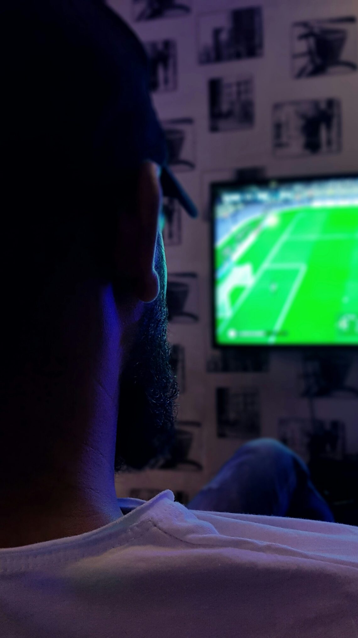 A person watches a soccer game on a wall-mounted TV in a dimly lit room.