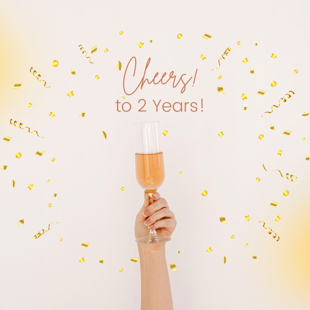 A hand raising a glass of champagne with "Cheers! to 2 Years!" text, surrounded by golden confetti.