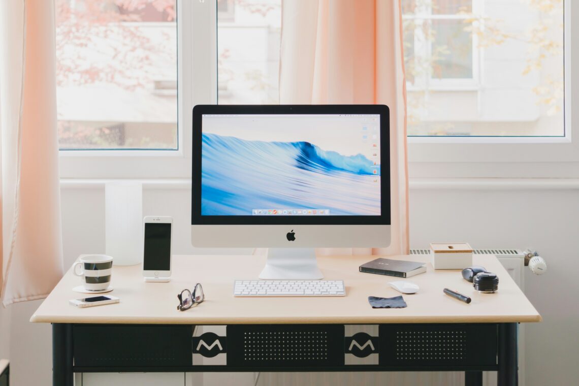 A tidy workspace with an iMac, smartphone, coffee cup, and office supplies on a desk.