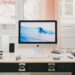 A tidy workspace with an iMac, smartphone, coffee cup, and office supplies on a desk.