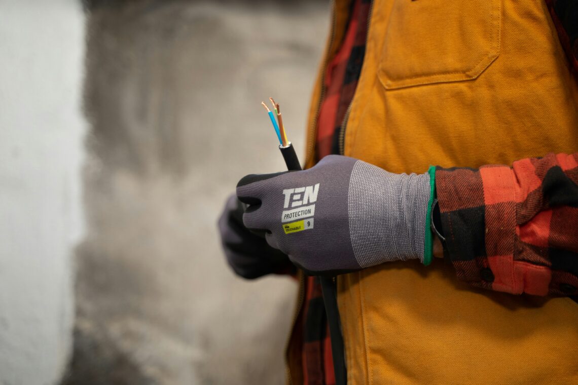 Person wearing a protective glove holding an electrical cable with exposed wires.