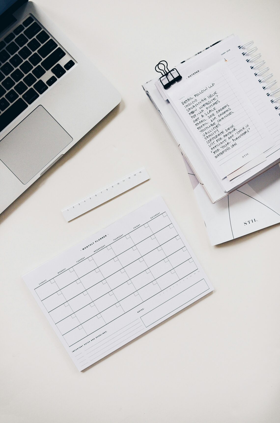 Laptop, planner with notes, ruler, and monthly calendar on a white desk.